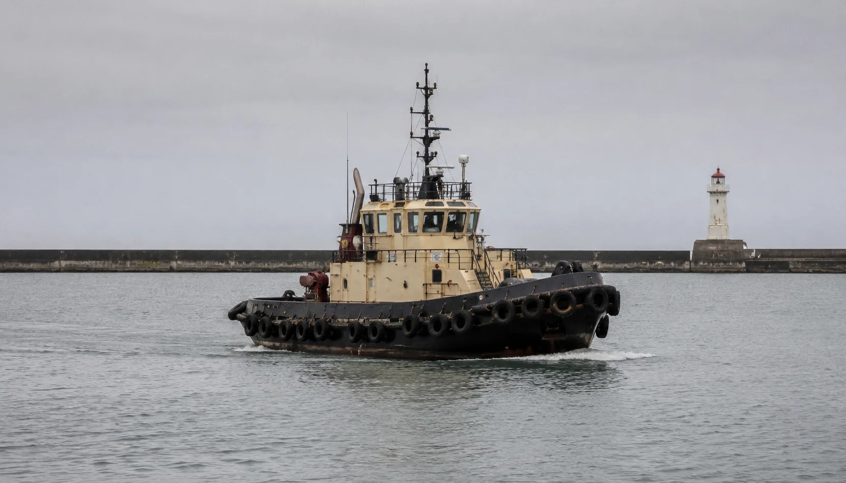 A harbor tug boat passing a lighthouse breakwater